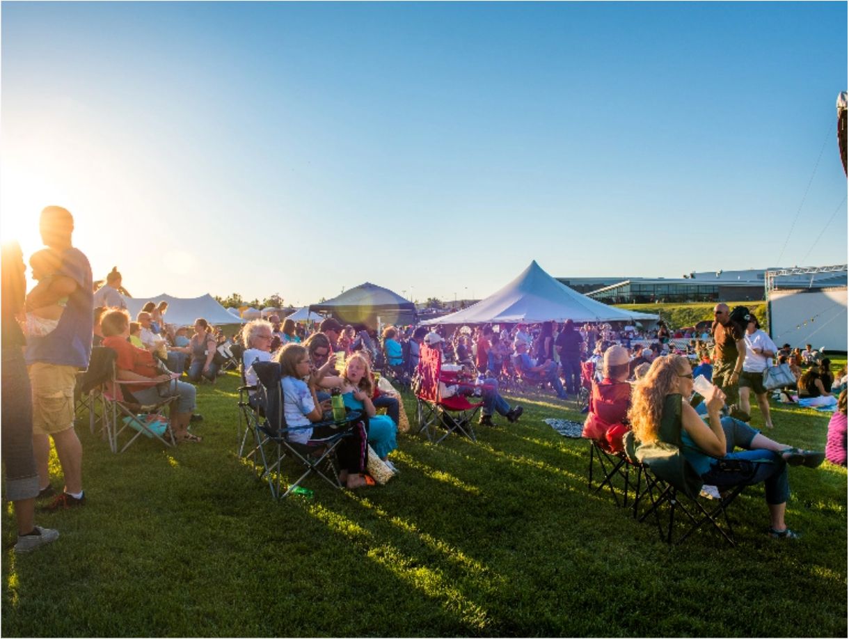 A large crowd of people sitting on the grass and in lawn chairs at an outdoor movie event.